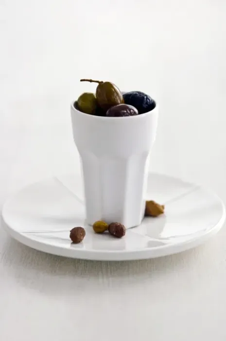 Framed Print : Mixed Italian olives in tall white ceramic pot on white plate with stones on white Framed Print : Mixed Italian olives in tall white ceramic pot on white plate with stones on white