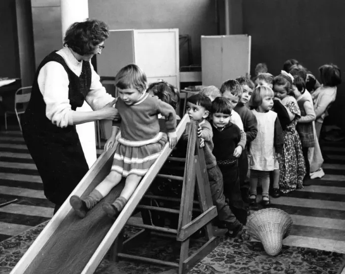 Framed Print : Mrs Joan Edison, leader of the nursery, helping her young charges on the slide Framed Print : Mrs Joan Edison, leader of the nursery, helping her young charges on the slide