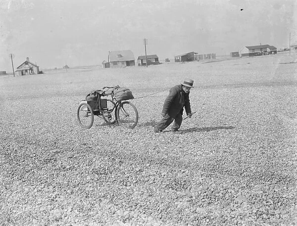 An old man pulling his tricycle along the shingle beach at Dungeness in Kent with