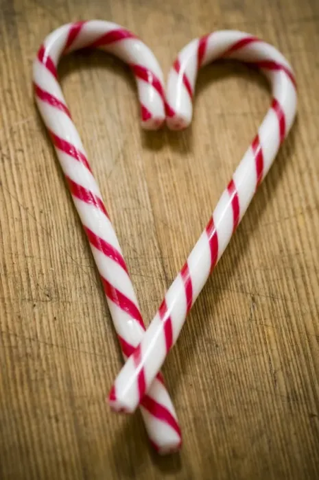 Framed Print : Two red and white striped candy canes on wooden surface crossed to make heart shape