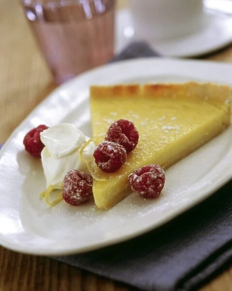 Slice of classic lemon tart served with fresh raspberries, lemon zest and creme fraiche credit