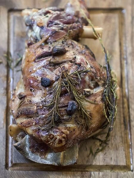 Slow roast shoulder of lamb with garlic and rosemary, on wooden carving board