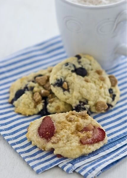 Soft cookies with berries and nuts on blue and white striped napkin with mug of cappucino credit