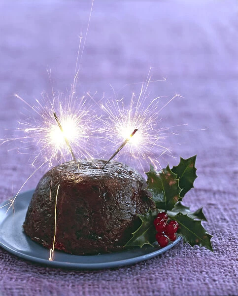 Traditional British Christmas pudding with with holly and berries and sparklers alight