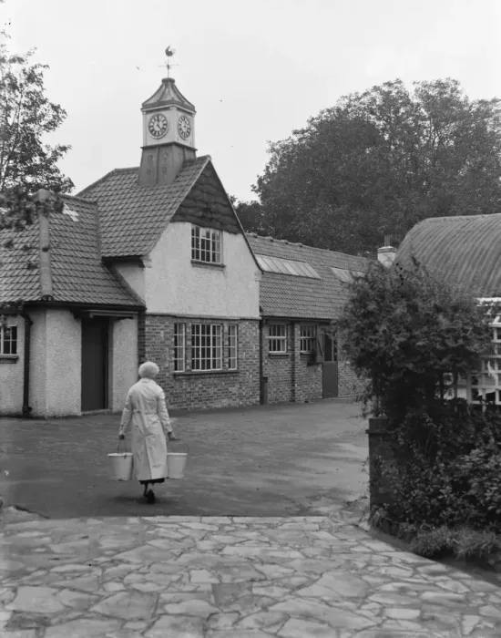 Framed Print : Woman carrying pails on a farm with new barn and clock tower. 1935