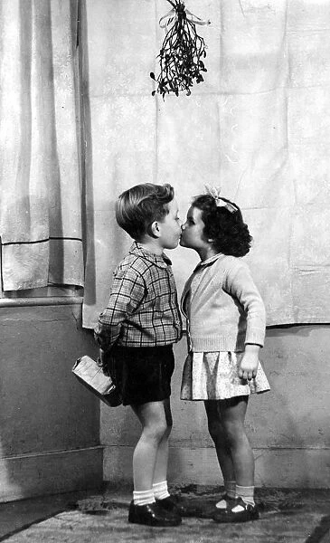 Young boy and girl kissing underneath the mistletoe at Christmas time 1956 love