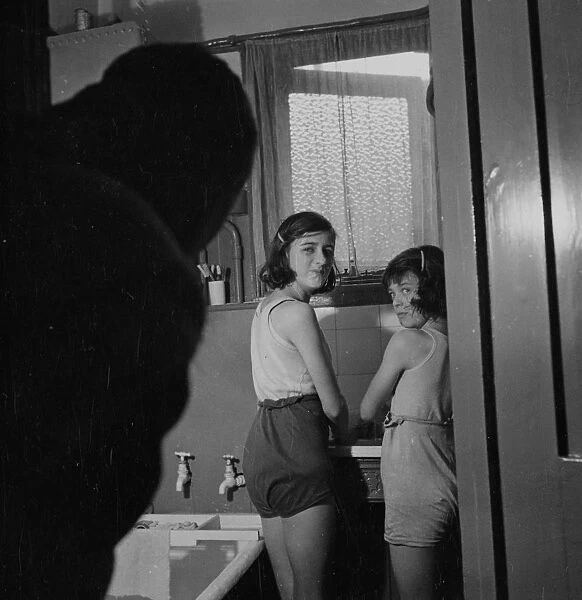 Two young girls in a bathroom, standing by a sink. [no caption, location or date]