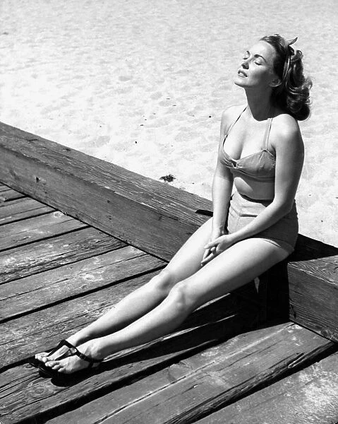 A young lady wearing a bikini and sandals sunbathing