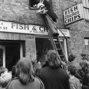 The bridegroom climbs a ladder to kiss his bride at the window above a fish and chip shop The bridegroom climbs a ladder to kiss his bride at the window above a fish and chip shop