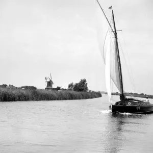 The Broads, Norfolk. Wherry sailing on a river / canal, a windmill in the background 1934