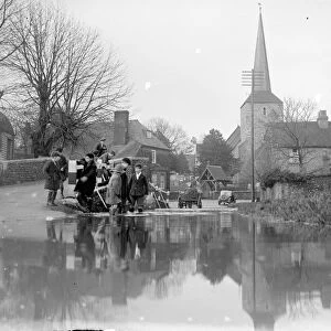 Children paddle in the flooded ford at Eynsford, Kent with St Martins church