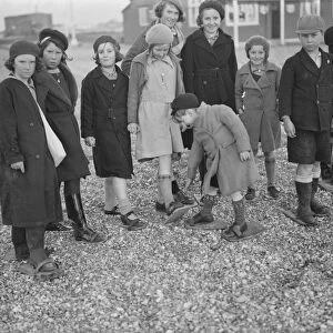 Children playing on the shingle beach at Dungeness. They use beach shoes to walk