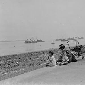 Children sit on the promenade at Gravesend river front and look out over the Thames
