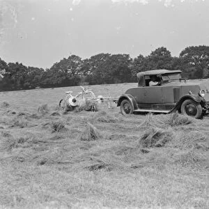 A farmer haymaking in a field using a car to pull the machinery. 1939