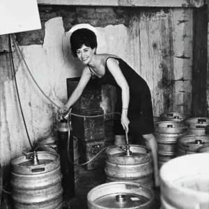 Le glamour dans la cave alors que la barmaid Lois tape un autre fût de bière. 19 octobre 1963. Le glamour dans la cave alors que la barmaid Lois tape un autre fût de bière. 19 octobre 1963.