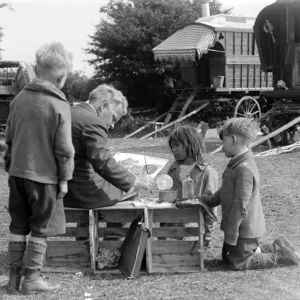 Gypsy children watching a man painting their caravan camp on Epsom Downs, Surrey