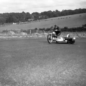 John Surtees hangs over the motorcycle side - car to balance the wheel as his father