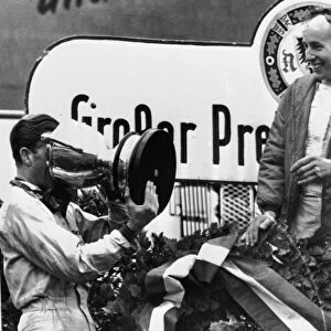 John Surtees looks smilingly on as Graham Hill drinks Champagne out of the Gian Cup