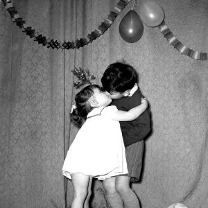 A little boy and girl kissing under the mistletoe at a Christmas party