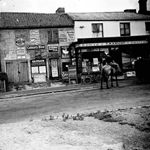 Man on horseback in front of grocers shop around Sevenoaks area, Kent. Advertisements and signs