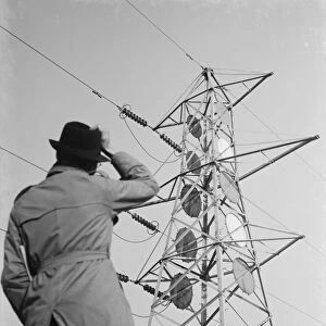 A man stands looking up at an electricity pylon in Shoreham, Kent. 1936