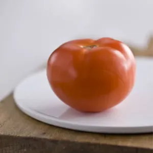 Single red tomato on white platter on wooden board credit: Marie-Louise Avery /