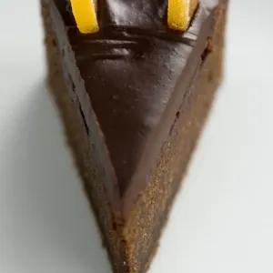Slice of rich dense dark chocolate cake with shiny choc topping and candied orange Slice of rich dense dark chocolate cake with shiny choc topping and candied orange