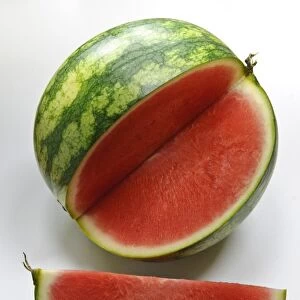 Small watermelon on white surface with quarter cut out showing red flesh credit