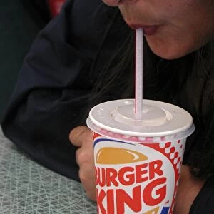 Sucking a soft drink out of a straw in a colourful Burger King disposable cup with a plastic lid
