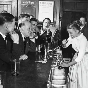 A woman barmaid pulls a pint of beer for male customers in a London pub, England. 1950s