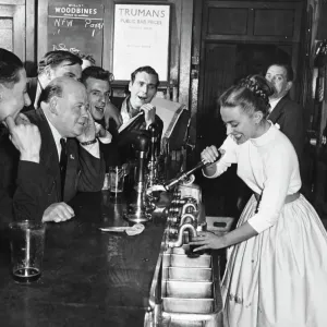 Une barmaid femme tire une pinte de bière pour des clients masculins dans un pub londonien, Angleterre. 1950s Une barmaid femme tire une pinte de bière pour des clients masculins dans un pub londonien, Angleterre. 1950s