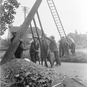 workers use ladders and poles erect an electric pylon next to a road in Trottiscliffe