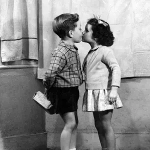 Young boy and girl kissing underneath the mistletoe at Christmas time 1956 love