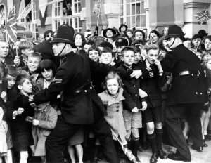 14 October 1938 Crowds of children, held back by policemen, cheering Queen Mary