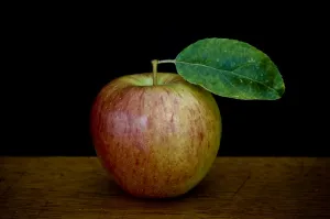Apple with leaf on wooden surface against black background credit: Marie-Louise