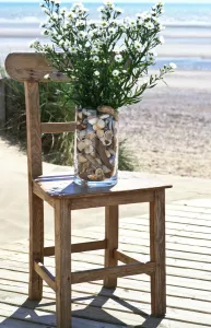 Chair Prints: Bunch of michaelmas daisies in pebble filled vase on old chair on decking by