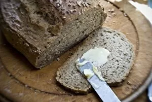 Food Collection: Buttering a slice of bread from a wholegrain, rye and walnut loaf on old wooden board