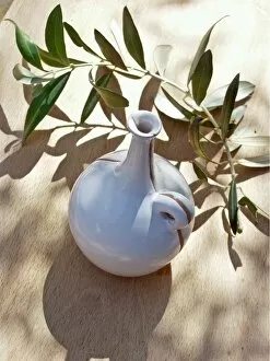 Leaves Collection: Ceramic oil bottle on tabled dappled in Italian sunshine with branch from olive tree