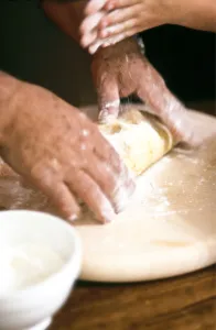 Chef kneading and rolling pastry with little girl helping - hands only shown credit