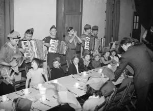 Musicians Prints: Children being entertained by an accordian band while they have their Christmas breakfast