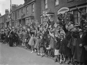 Crowds stand at the side of the road and cheer for the Duchess of Kent