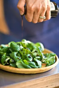 Drizzling balsamic vinegar onto lambs lettuce in pottery dish. credit: Marie-Louise
