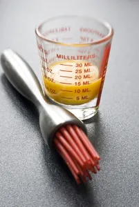Utensils Prints: Egg yolk in small glass measuring glass with modern pastry brush with red silicone