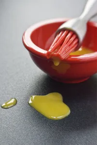 Egg yolk in small red bowl and dripping off red silicone bristles of modern pastry