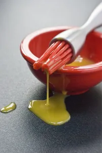 Egg yolk in small red bowl and dripping off red silicone bristles of modern pastry