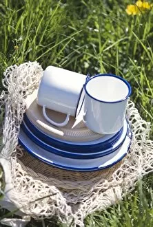 Outdoor Outdoors Collection: Enamel and paper cups and saucers piled up on a string bag on the grass - part of