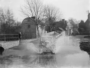 Drive Prints: Eynsford Bridge flooded. A car ploughs through the water. 1937