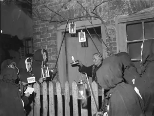 Fence Prints: An Eynsford resident has a visit from hooded carol singers. 1935