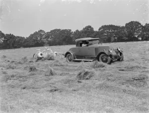 A farmer haymaking in a field using a car to pull the machinery. 1939