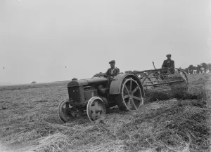 Farmers using a new tractor drawn haymaking machine on a field in Farningham, Kent
